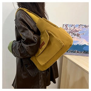 Vue de profil d'un sac messager en toile jaune gingembre avec étiquette en cuir porté