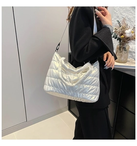 Close-up of white glossy quilted puffer tote bag with black strap and padded texture