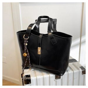 Détail d'un sac cabas en cuir noir brillant avec boucle dorée sur une valise