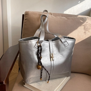Sac fourre-tout argenté chic avec fermoir doré posé sur un canapé beige élégant