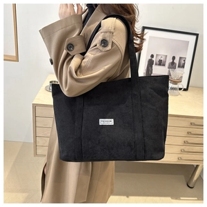 Detail of black corduroy tote bag with fashion label carried by a model in a trench coat