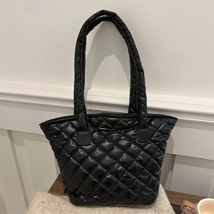 Quilted black tote bag with shoulder straps displayed on a wooden surface in a cozy room