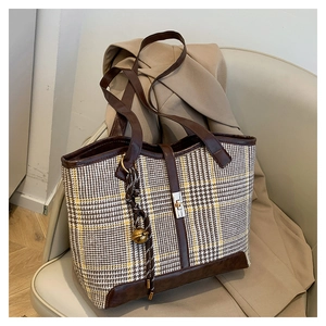 Detail of vintage houndstooth tote bag with brown leather trim and gold bell charm on a sofa