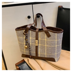Close-up of vintage houndstooth tote bag with brown leather trim and gold bell charm