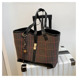 Detail of houndstooth tote bag with gold swivel lock and bell charm on leather trim