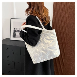 Dettaglio di una borsa tote trapuntata bianca lucida con ampi spallacci indossata da modella