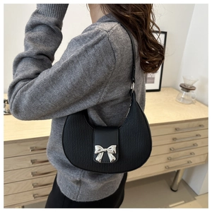 Detail of a black crescent hobo bag with a silver bow clasp on a grey knit sweater