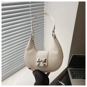 Detail of cream pleated leather underarm bag with silver bow buckle on white ledge