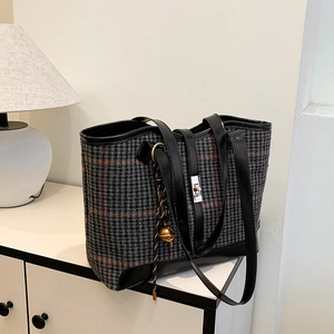 Retro houndstooth tote bag with leather trim and bell charm on a white desk