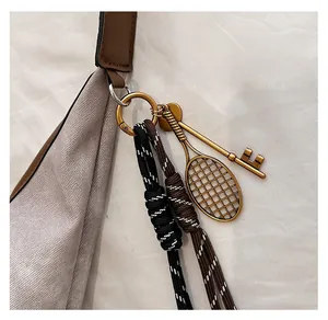 Detail of vintage gold tennis racket bag charm with braided cords on a handbag hook