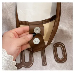Close-up of the metal magnetic clasp and retro letter patch on the canvas tote bag