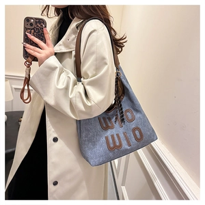 Detail of blue denim tote bag with leather letters and brown straps on beige coat