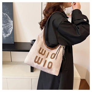 Detail of beige tote bag with brown leather trim, fringe tassel, and WIO WIO logo