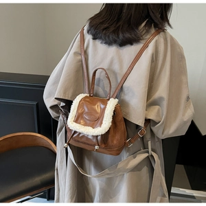 Détail d'un mini sac à dos marron foncé avec bordure en fausse fourrure blanche et écusson
