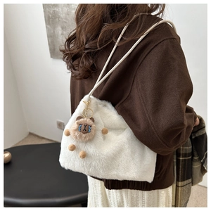 Detail of white plush shoulder bag with brown bear charm on a female model
