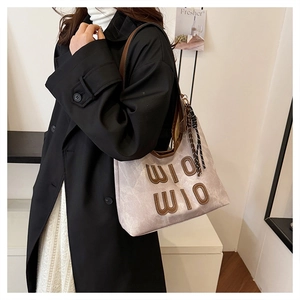 Detail of large tote bag showing textured cream fabric, brown leather trim and tassel charm