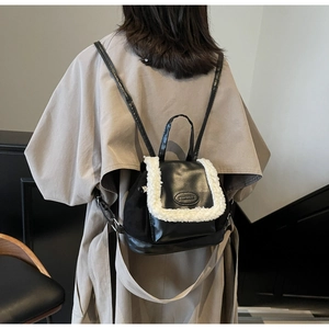 Mini black backpack with white faux fur trim shown on a model wearing a beige coat