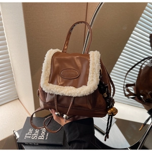 Detail of suede crossbody bag with fluffy faux fur trim and gold bell accessory