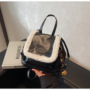 Detail of small black faux suede backpack featuring white fur trim and golden bell charm