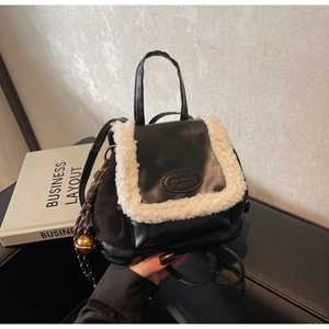 Detail of black faux leather backpack with white plush trim and golden bell charm