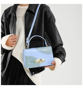 Detail of light blue crossbody bag with crocodile texture and gold hardware clasp
