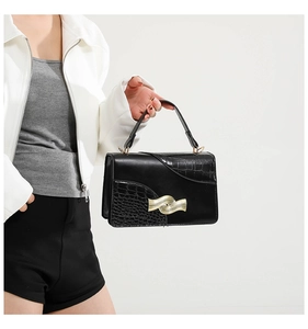 Close-up of black crocodile-embossed faux leather bag with golden wave-pattern buckle
