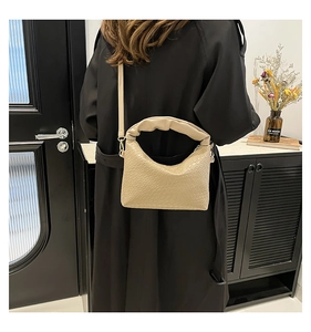 Detail of beige woven texture and ruched handle on a stylish crossbody dumpling bag