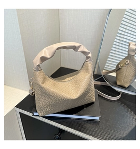 Detail of beige woven texture handbag with pleated handle on book reflected in mirror