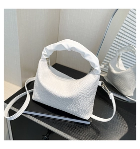 Detail of white woven crescent bag featuring a ruched cloud handle and metallic hardware