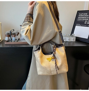 Close-up of beige suede bucket bag with brown leather trim and golden bell pendant