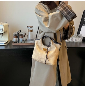 Detail of a luxury bucket bag featuring a gold triangle emblem and woven rope accents