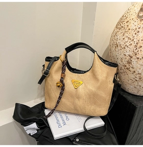 Detail view of khaki bucket bag featuring triangular logo and decorative bell charm