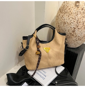 Detail showing khaki suede bucket bag with black leather trim and yellow triangle plaque