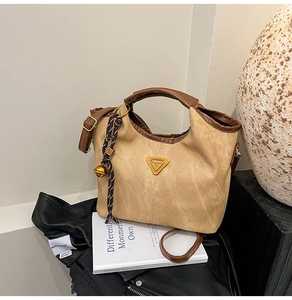 Detail of camel bucket bag with leather trim and gold bell charm on black jacket