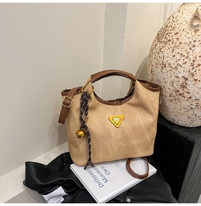 Detail of khaki canvas bucket bag with brown leather trim and metal logo plaque