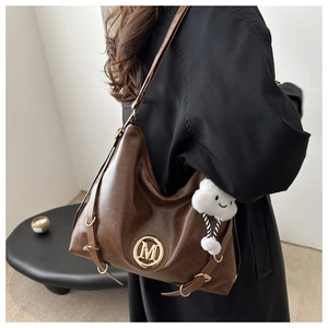 Detail of a brown leather hobo bag with gold metal logo and white plush cloud charm