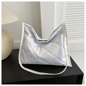 Detail of white quilted tote bag with diamond pattern and leather straps on black desk