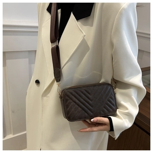 Detail view of dark coffee small crossbody bag with V-shaped quilting on a white blazer