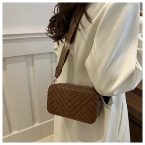 Detail of a brown rectangular crossbody bag featuring V-shaped quilting and wide strap