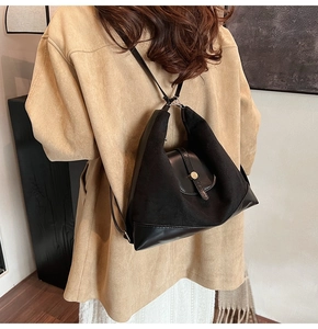 Detail of black textured leather bag with gold buckle on a model in a trench coat