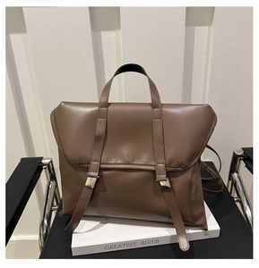 Detail of dark brown leather handbag with gold metal hardware on office desk setup