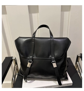 Detail of matte black leather bag featuring silver metal buckles on a black chair