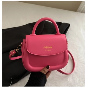 Detail of pink PU leather saddle bag featuring gold fashion logo and rounded handle