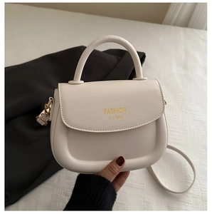 Close-up of cream leather shoulder bag featuring gold fashion lettering and rounded handle