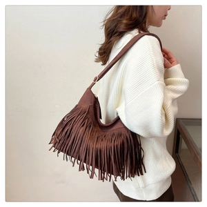 Detailed view of coffee brown suede shoulder bag with long bohemian tassels on a model