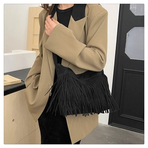 Detail of black suede crossbody bag featuring long fringes styled with a khaki blazer