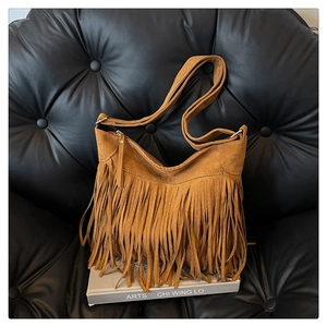 Close-up of brown suede fringe bag with golden zipper on a vintage leather sofa