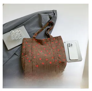 Detail shot of brown corduroy tote bag featuring red strawberry prints and functional pocket