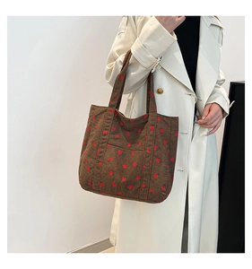Close-up of brown corduroy tote bag with strawberry embroidery worn with a beige coat
