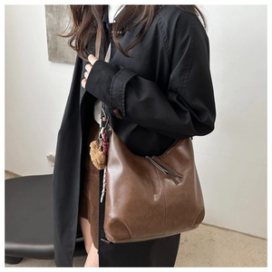 Detail of dark brown leather hobo bag with plush ball charm shown on model's shoulder